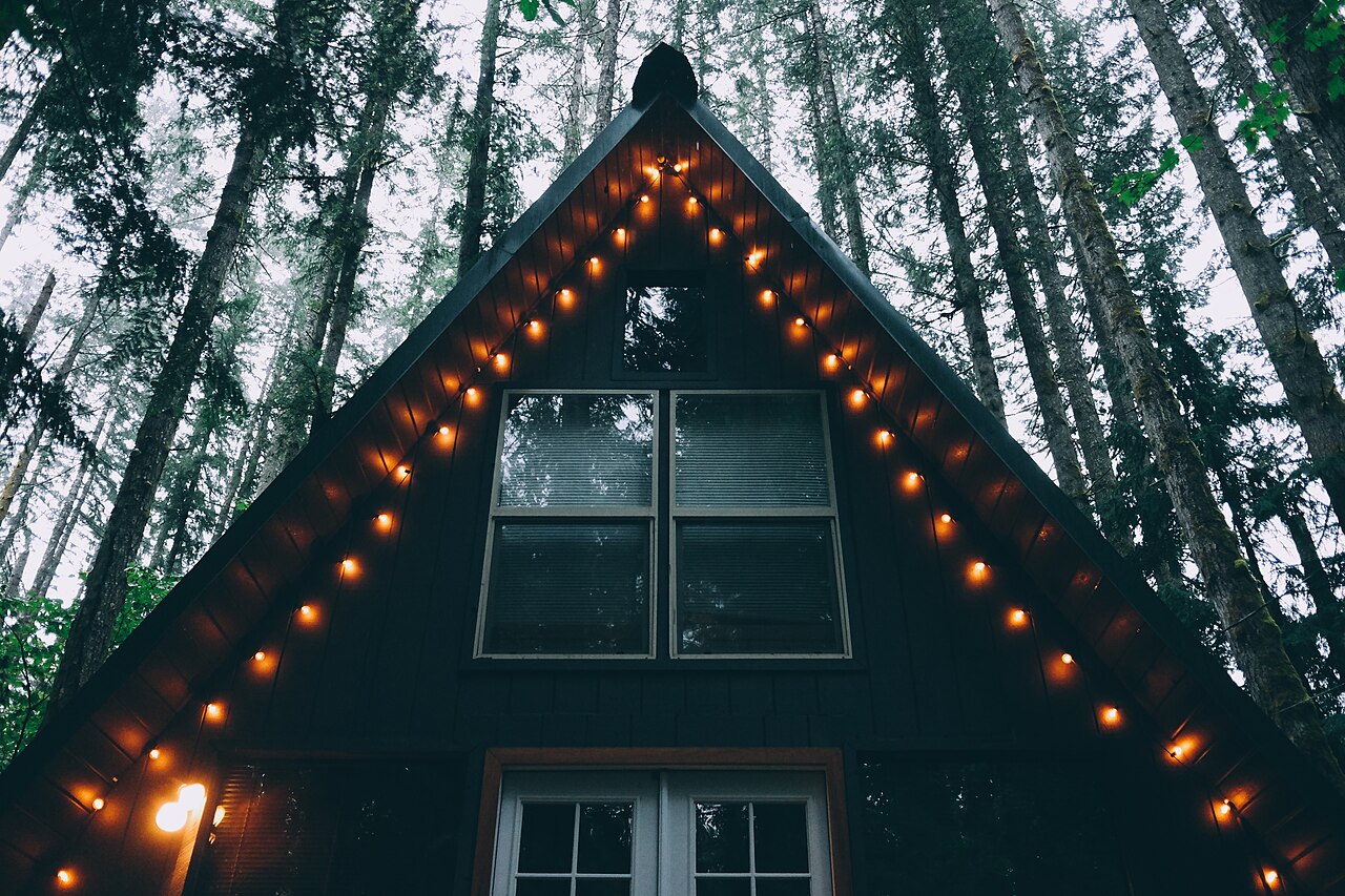 A-Frame-Hütte mit Lichterkette zwischen hohen Nadelbäumen